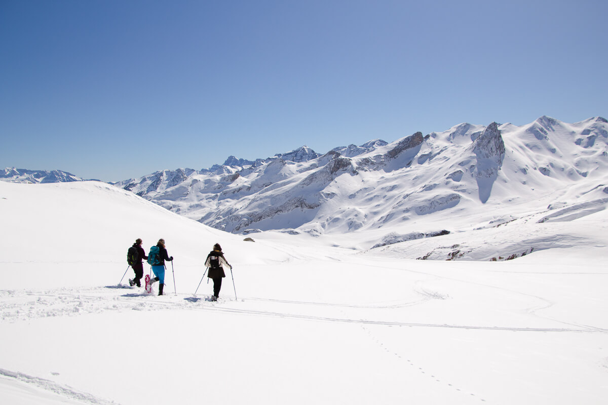 Women snowshoeing across a snowy mountain landscape under blue skies