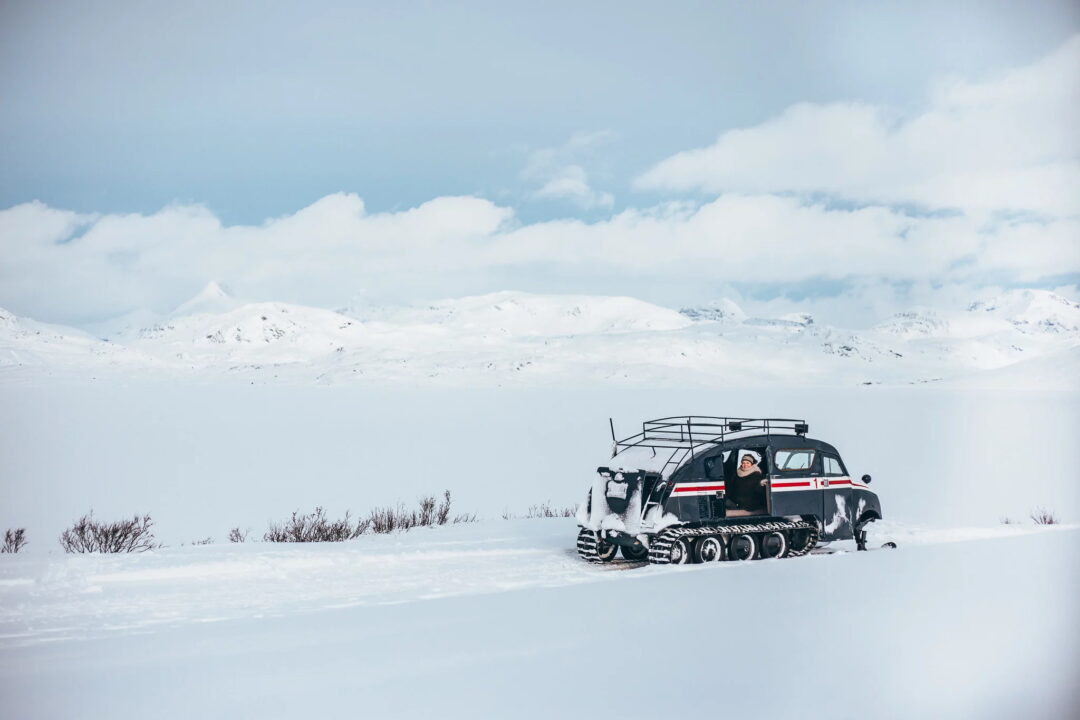 Tracked snow vehicle on a snowy mountain landscape with distant peaks in Norway