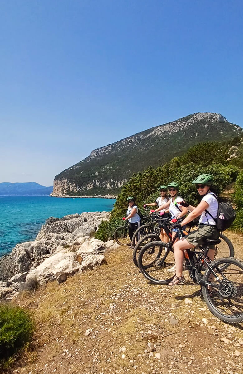 Women e-bike riders on a rocky coastline with sea and mountains in the background