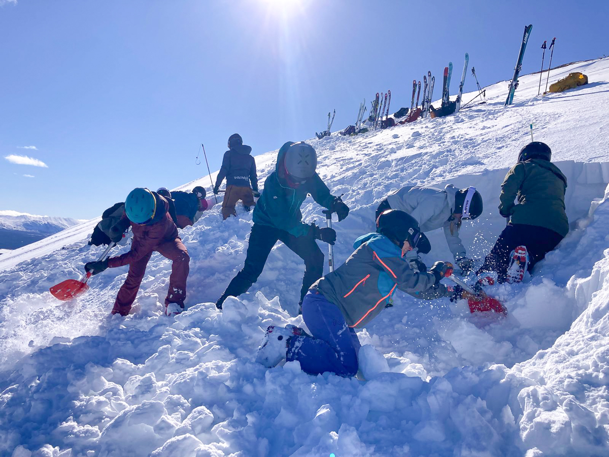 Women ski touring on a snowy mountain slope with skis and poles in bright sunshine.