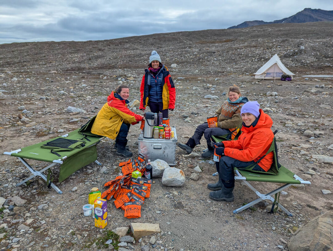 Women camping in Svalbard during a summer expedition, with tents and supplies on a rocky Arctic campsite