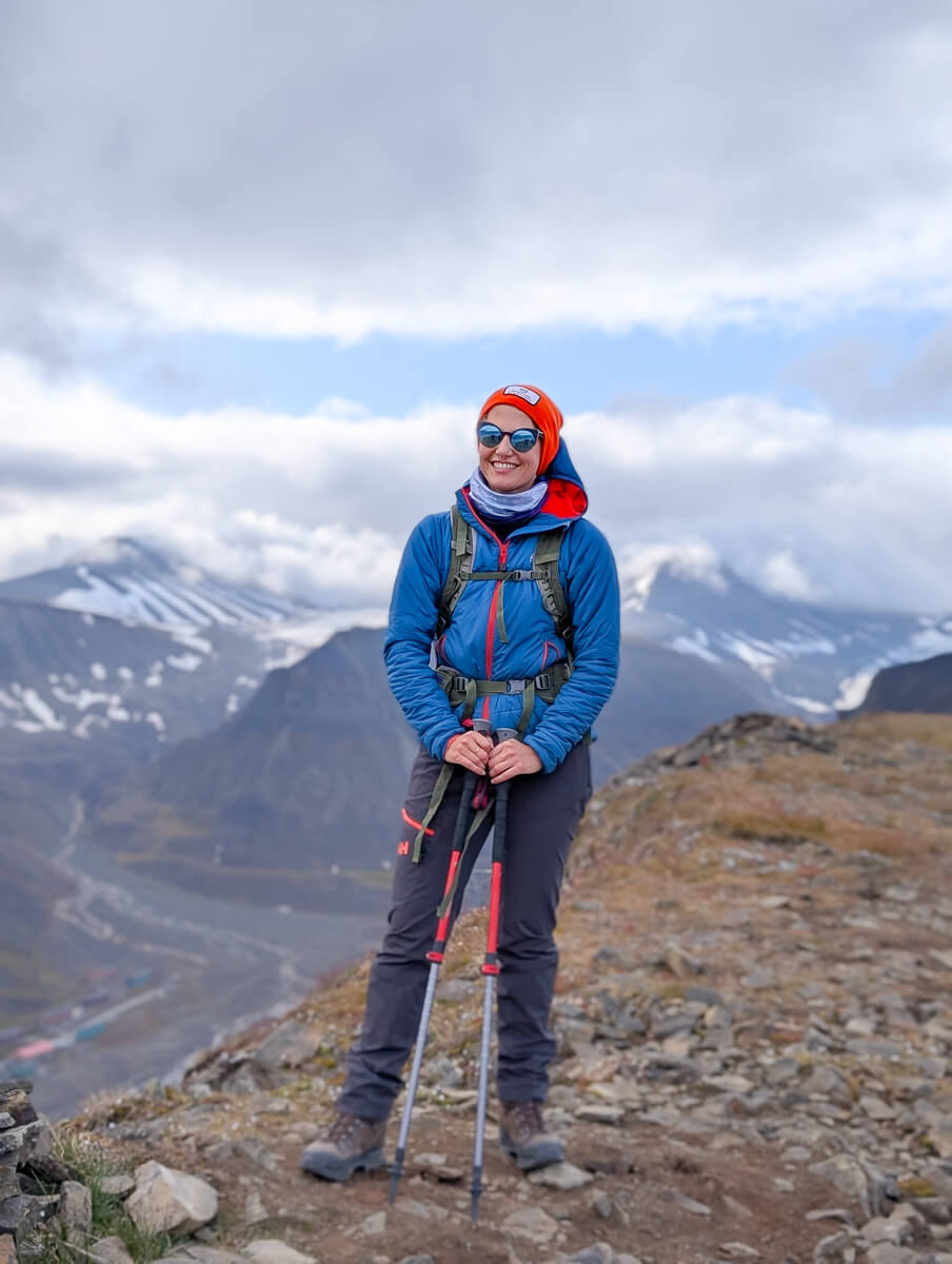 Woman trekking in blue winter gear with hiking poles in the mountains of Svalbard