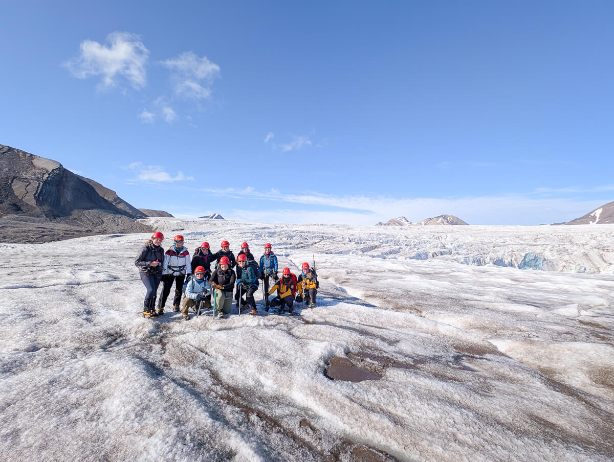 Women in expedition gear posing on a glacier with snowy mountains in Svalbard during a summer wilderness trip