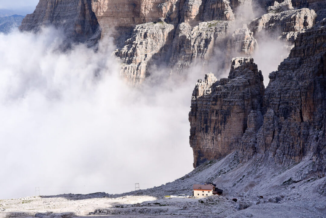 Dolomites mountain cliffs with low cloud and a small hut in the Italian Alps, Italy