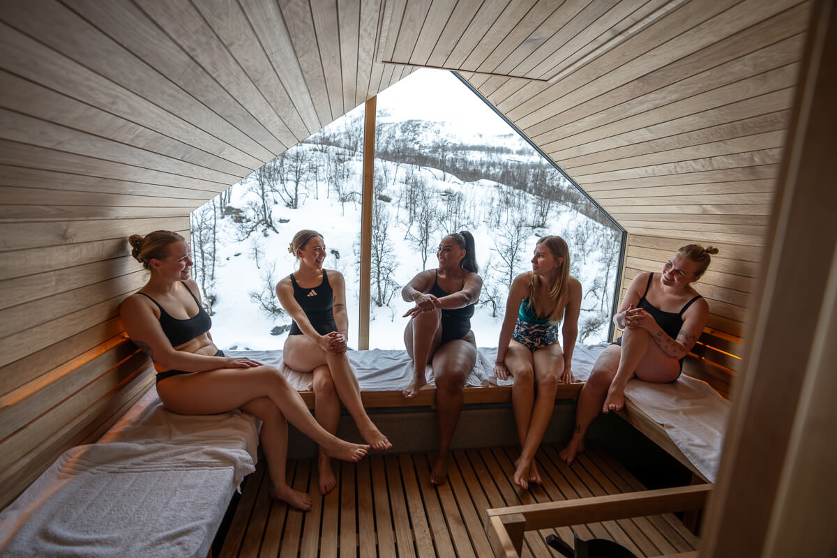 Women relaxing in a wooden sauna with a snowy mountain view through the window