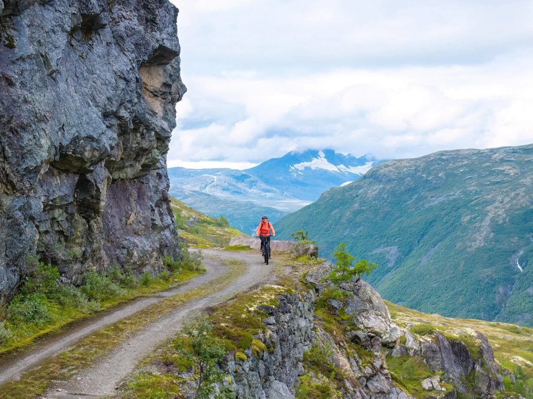 Woman hiking along a mountain path beside a rocky cliff in Norway’s scenic valleys