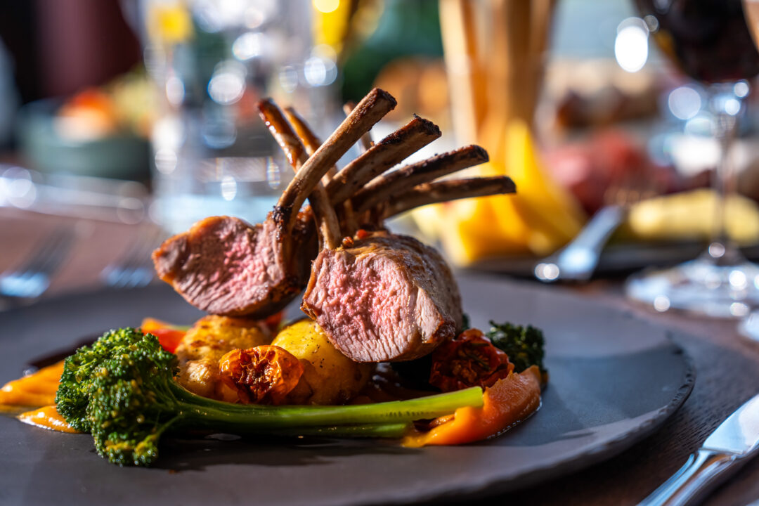 Rack of lamb with roasted vegetables on a plate, served at a restaurant dinner table