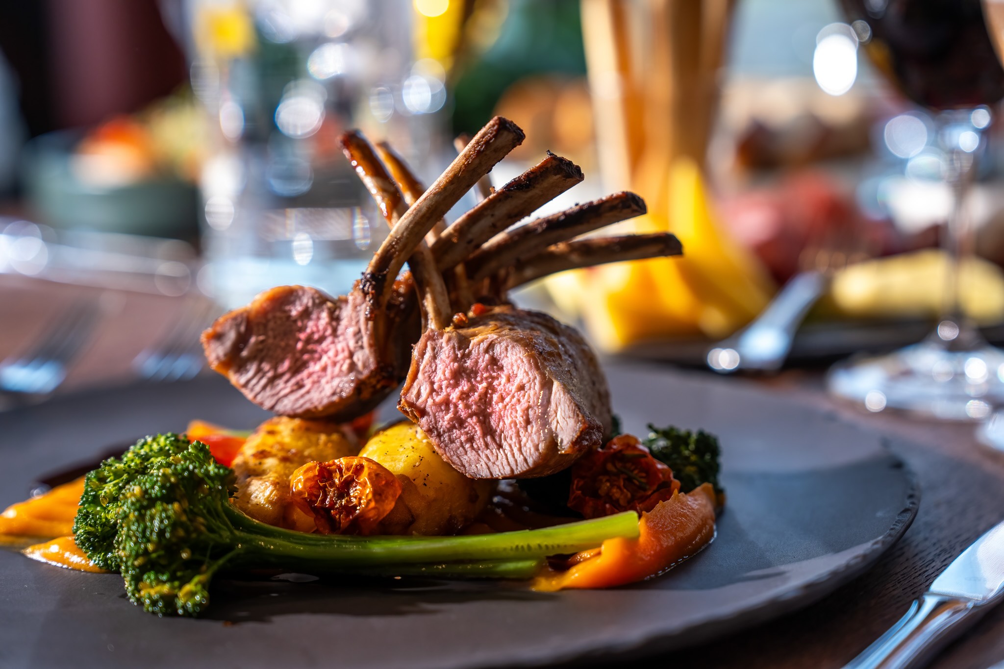 Lamb chops with vegetables on a restaurant plate, with a glass of water in the background