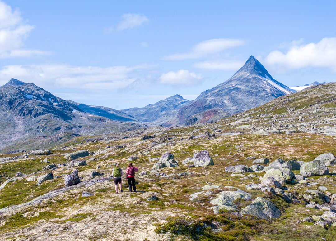 Women hiking on a mountain trail overlooking Jotunheimen, Norway under a blue sky