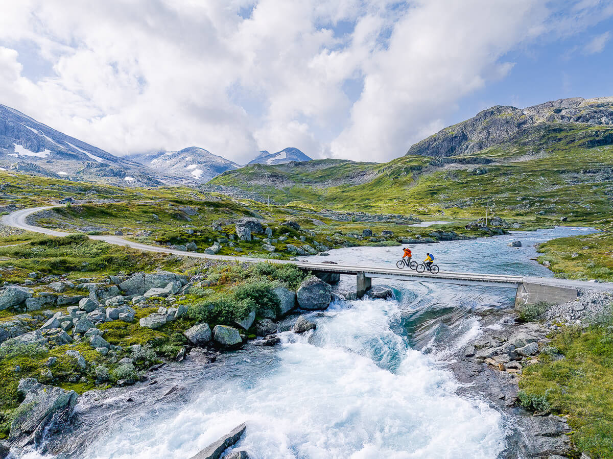 Mountain bike crossing a stone bridge over a fast river in a Norwegian mountain valley landscape