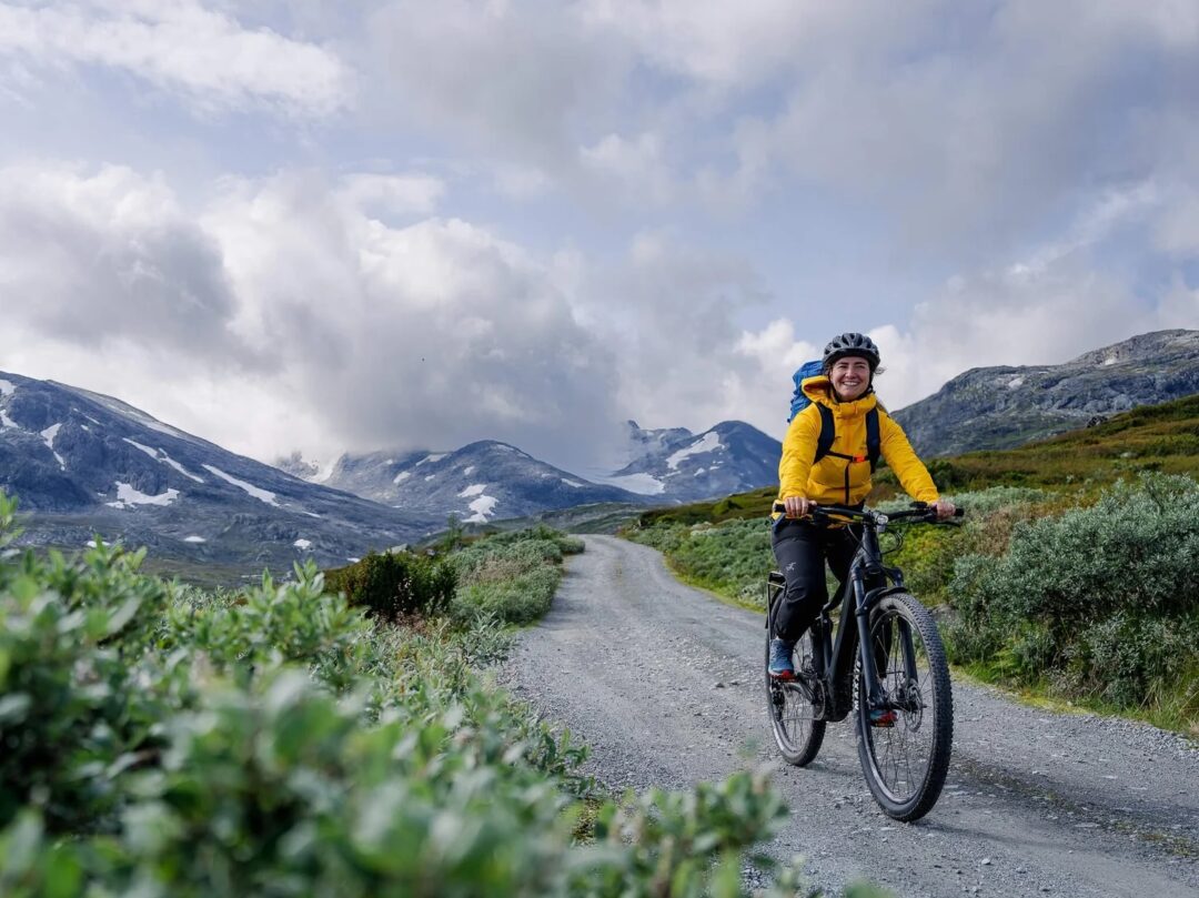 Woman mountain biking on a gravel road through alpine mountains, scenic adventure landscape