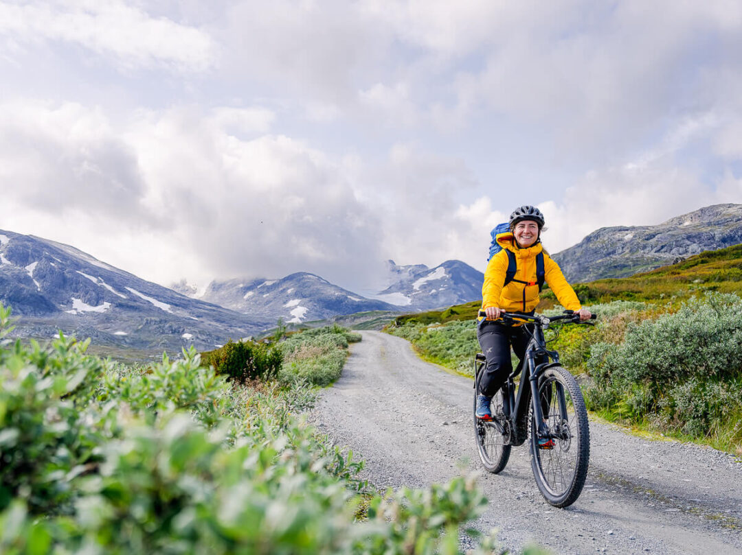Women mountain biking on a gravel track through Jotunheimen National Park with mountains under a cloudy sky