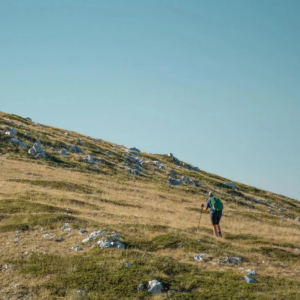Woman hiking on a grassy mountain trail across rocky hillsides