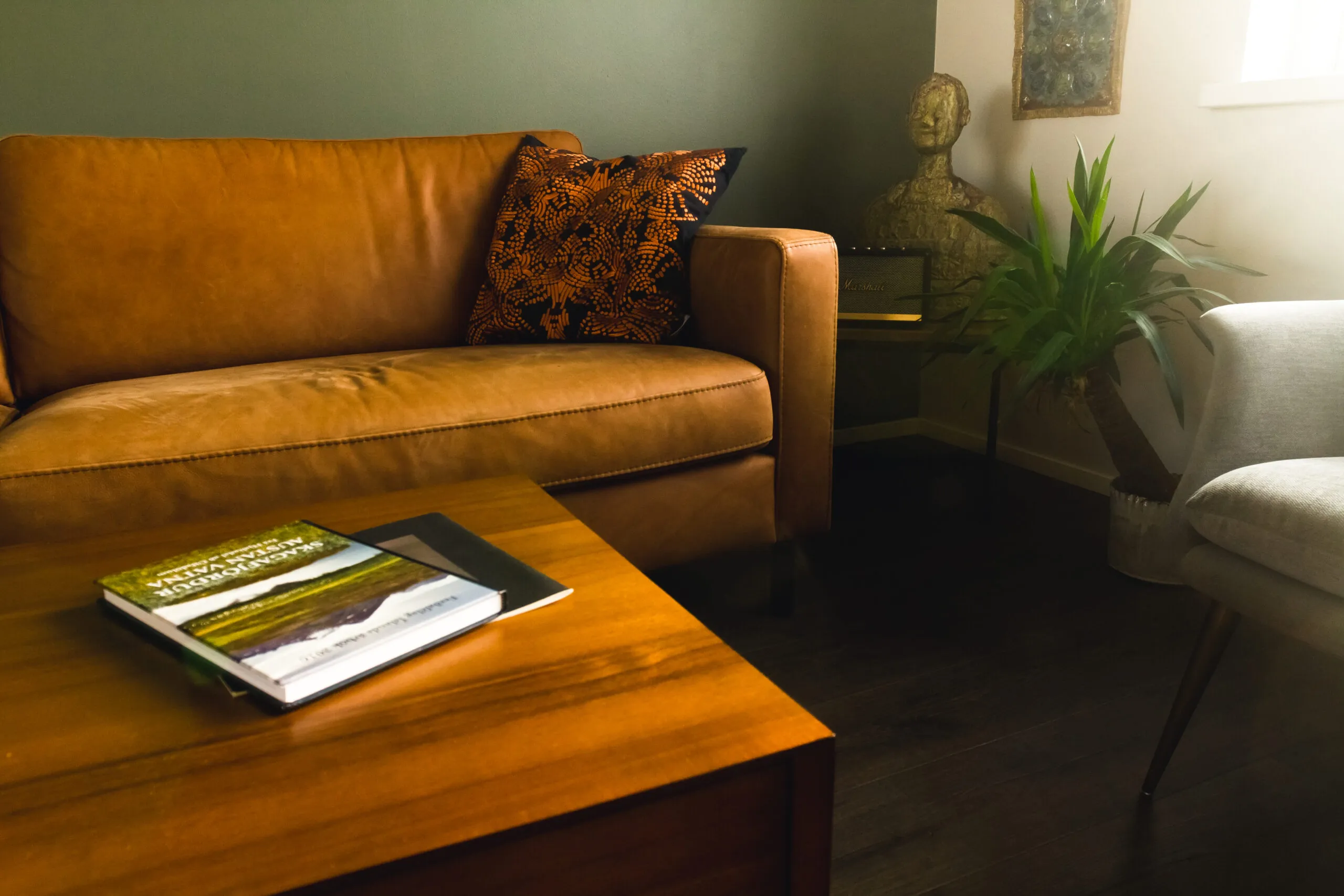 Living room lounge with mustard sofa, coffee table with books, and wall artwork indoors