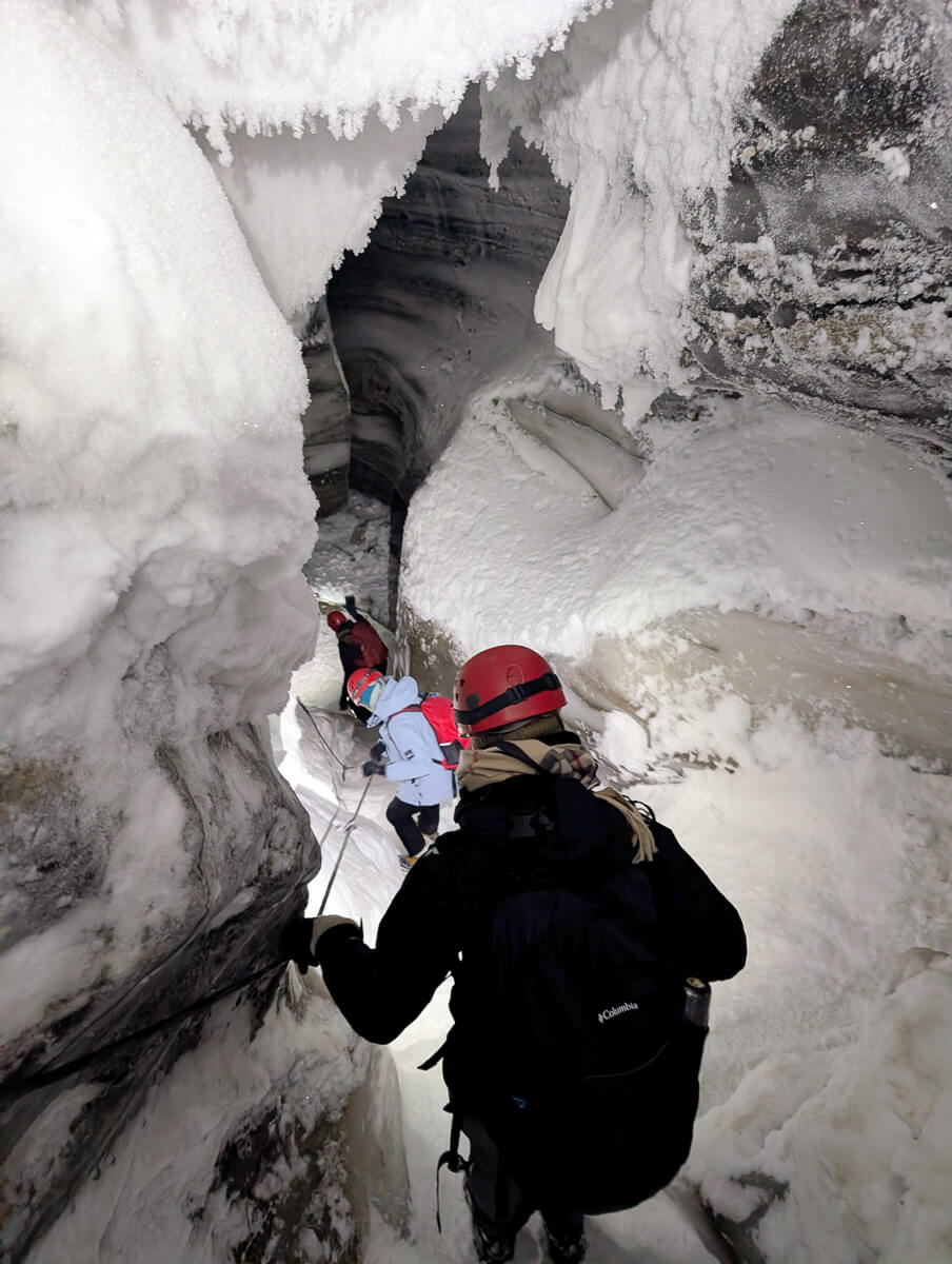 Woman in winter gear walking through a narrow snowy tunnel in the snow.