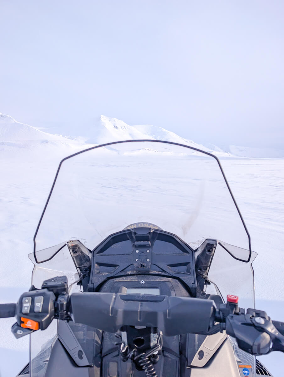 Snowmobile handlebars on snowy Svalbard landscape, view from the rider in a snowmobiling expedition