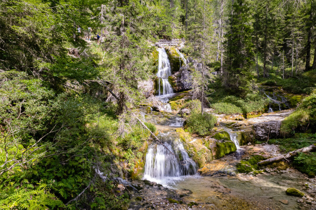 Multi-tier waterfall cascading through a lush forest landscape with a winding stream