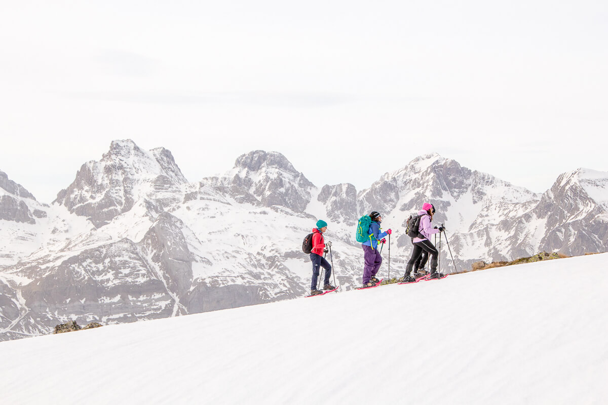 Snowshoeing hikers on a snowy mountain slope with alpine peaks in winter