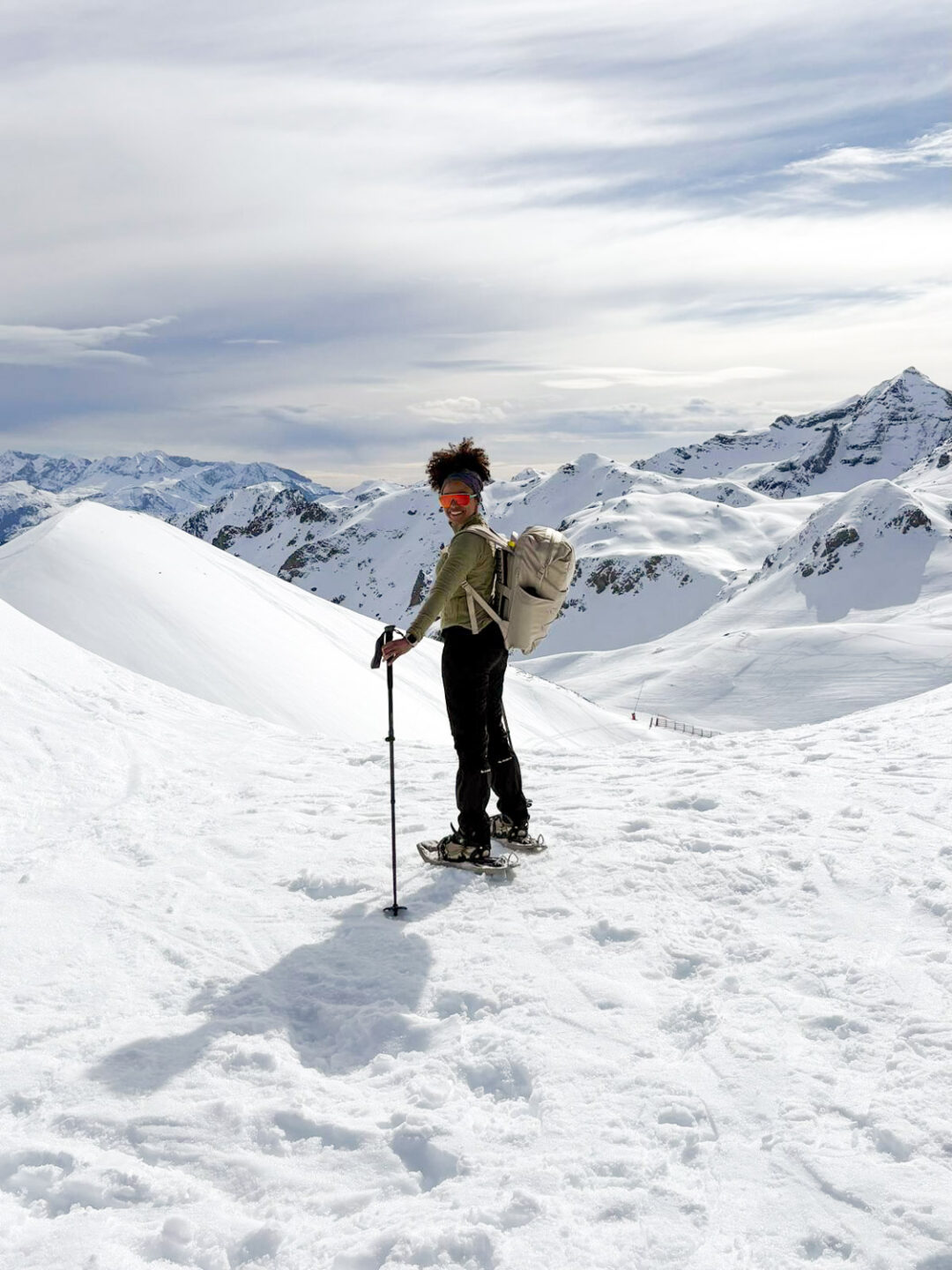 Woman skiing with poles across snowy mountain slopes under a cloudy alpine sky