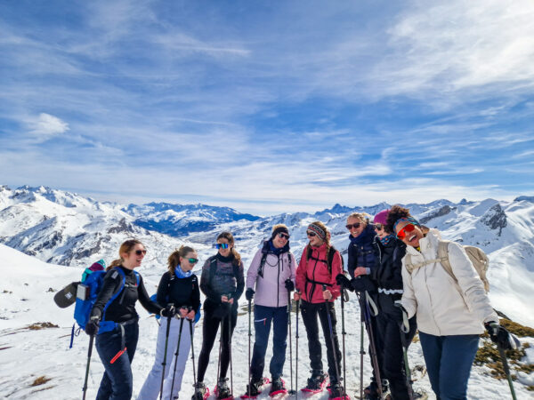 Women winter hikers with trekking poles on a snowy mountain ridge under blue sky