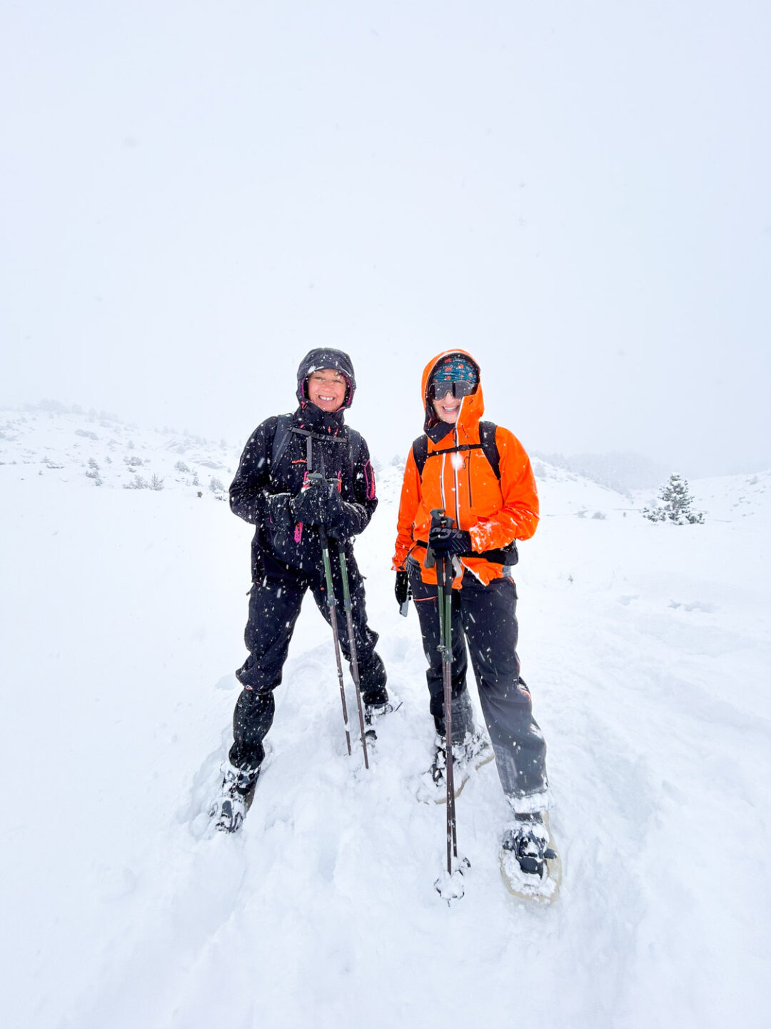 Two women snowshoeing in snowy mountains under clear winter skies
