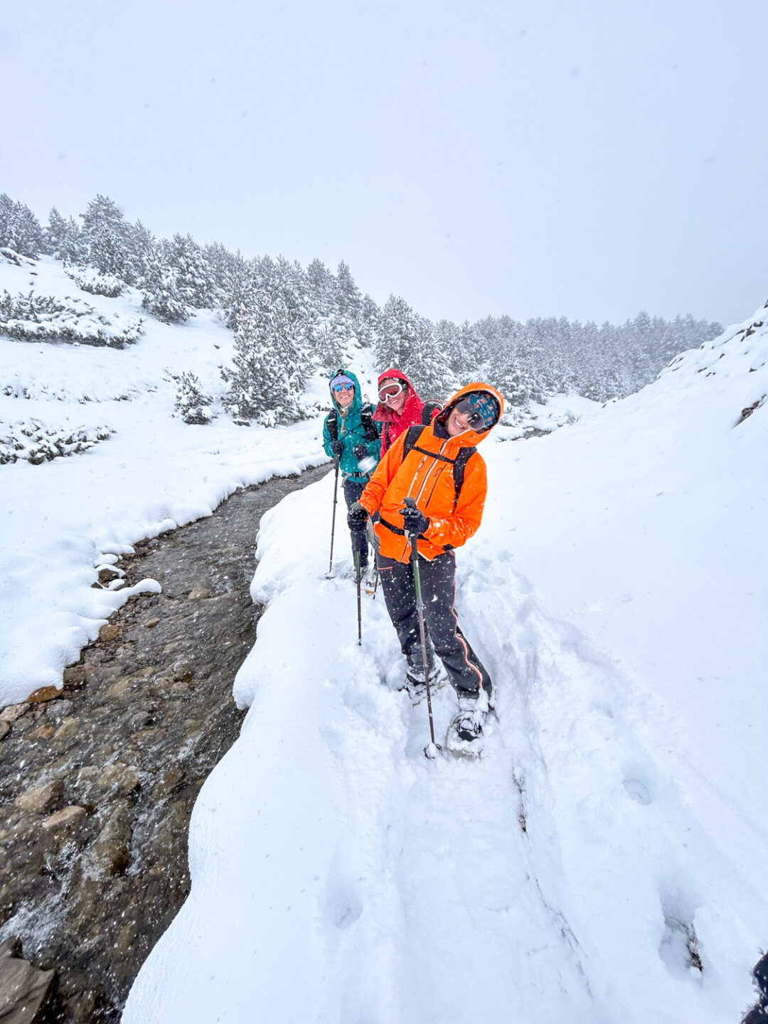Women snowshoeing along a snowy mountain trail beside a winter stream