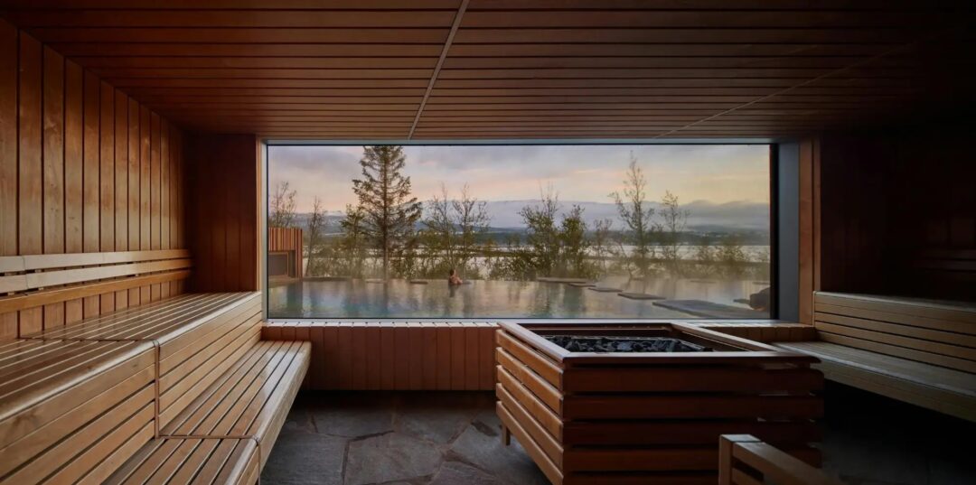 Wooden sauna interior with hot tub and large window looking out over a snowy landscape