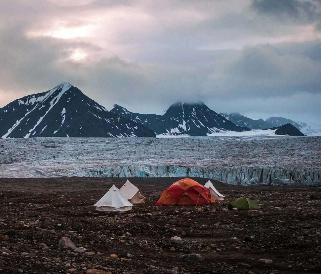 Camping tents beside a glacier with snowy mountains in Svalbard, Arctic wilderness expedition