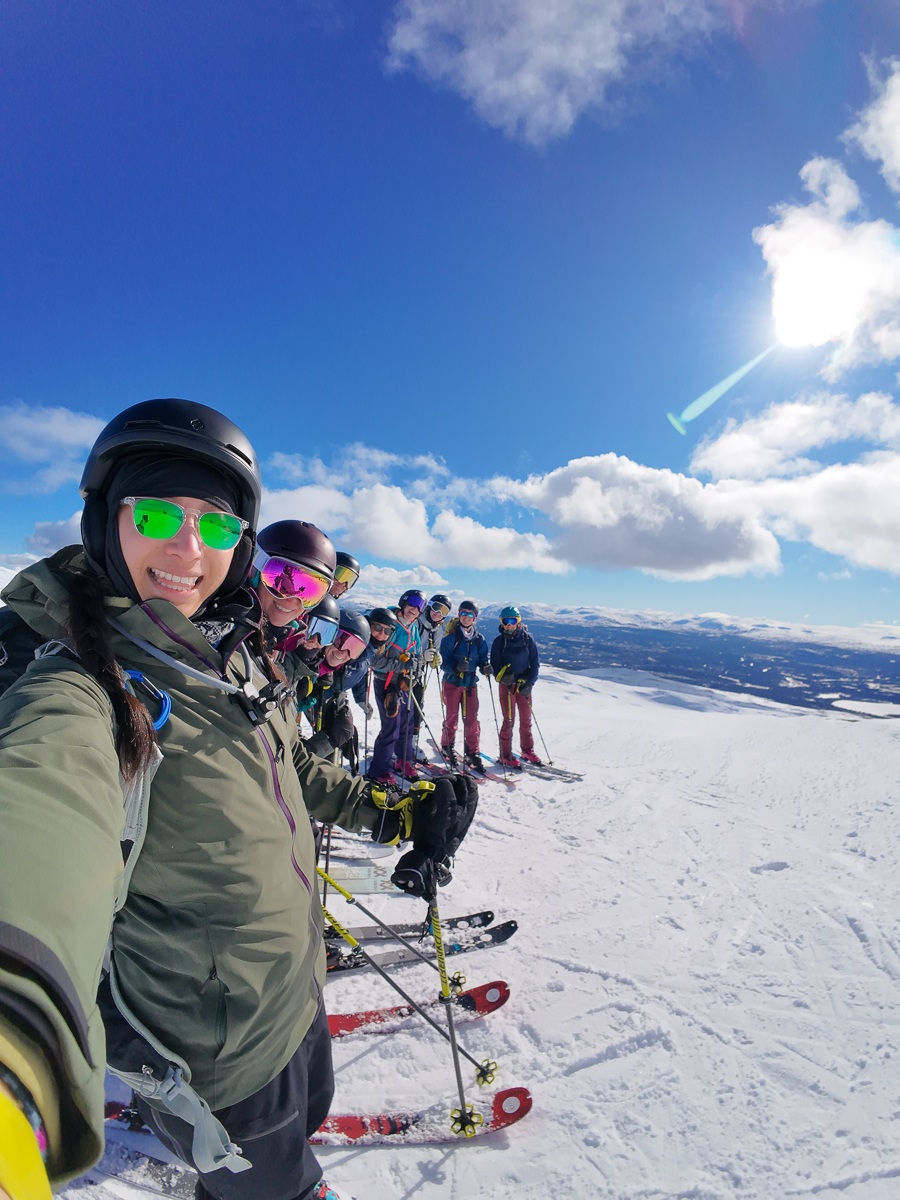 Women ski touring on snowy slopes with a group on skis under a bright blue sky