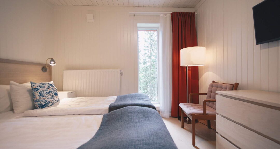 Cozy bedroom with two beds, window and red curtains, suitable for a wilderness adventure stay