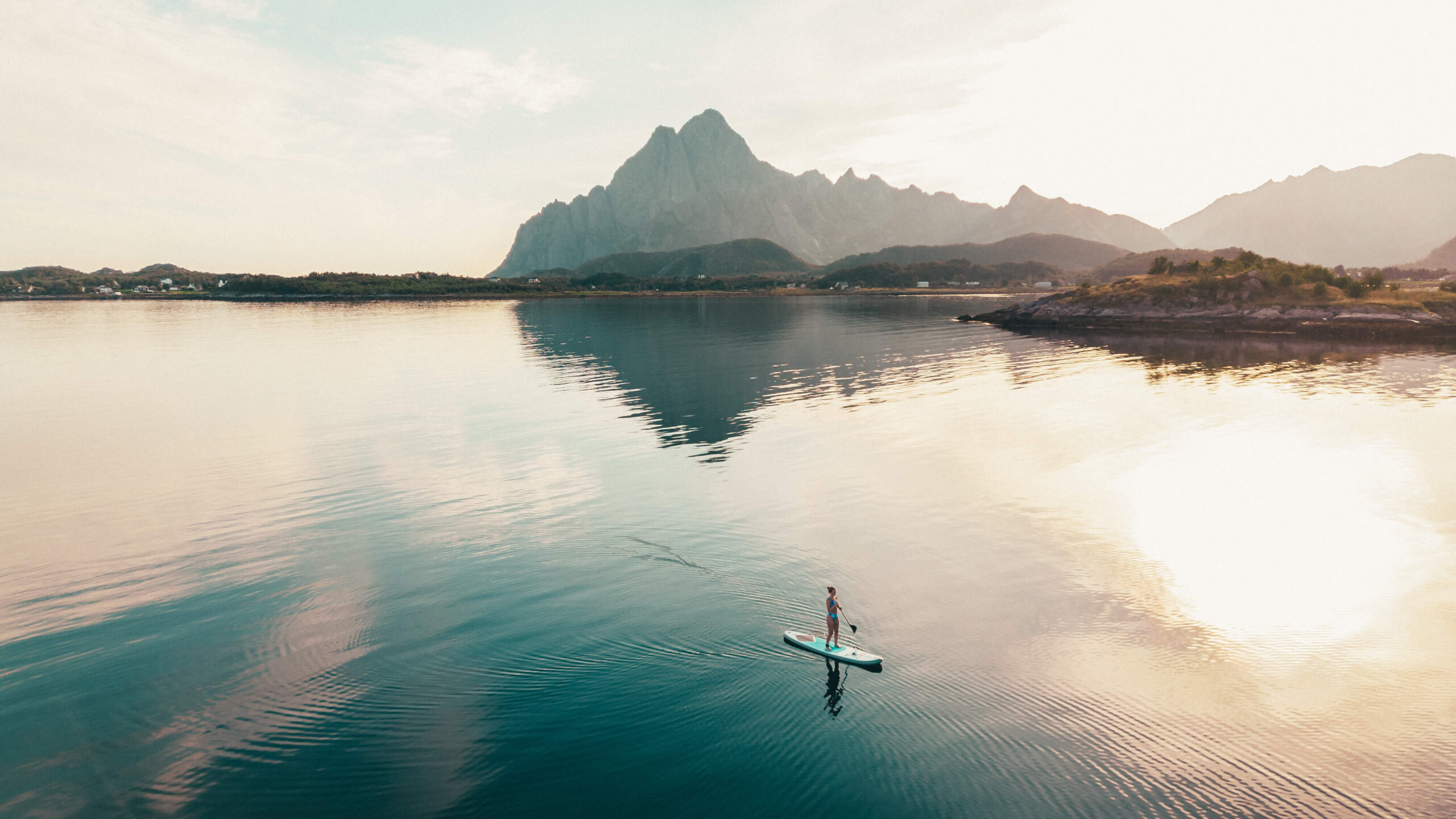 Woman paddleboarding on still waters in Lofoten, Norway, at sunrise with mountains in view