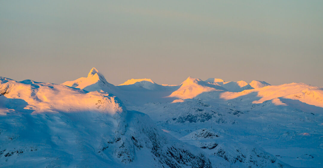 Snow-covered Norwegian mountains at sunset, showing a vast alpine landscape for a skiing holiday in Norway