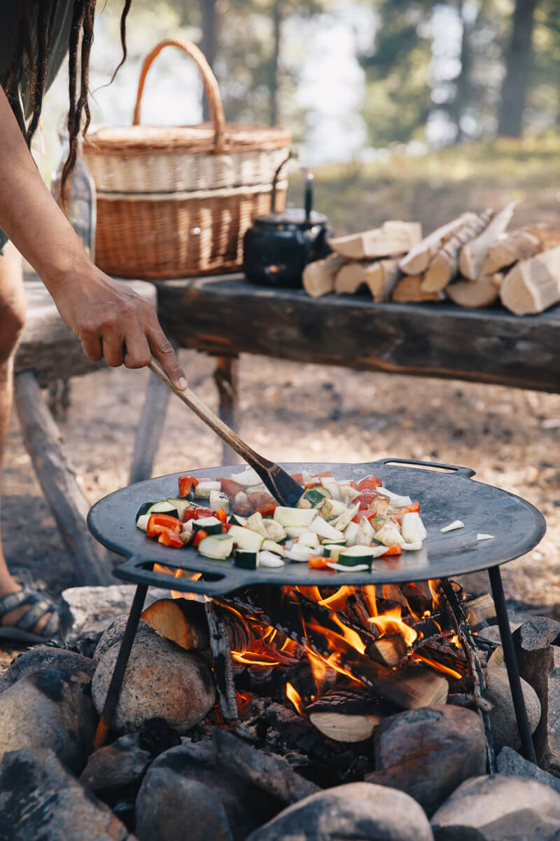 Women cooking vegetables on a campfire at outdoor meal in Swedish Lapland wilderness, with frying pan.