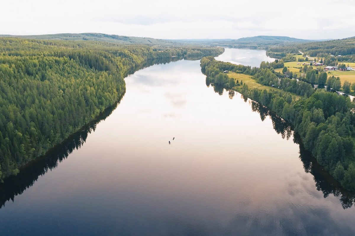 Aerial view of a wide river through forest and hills in Swedish Lapland wilderness