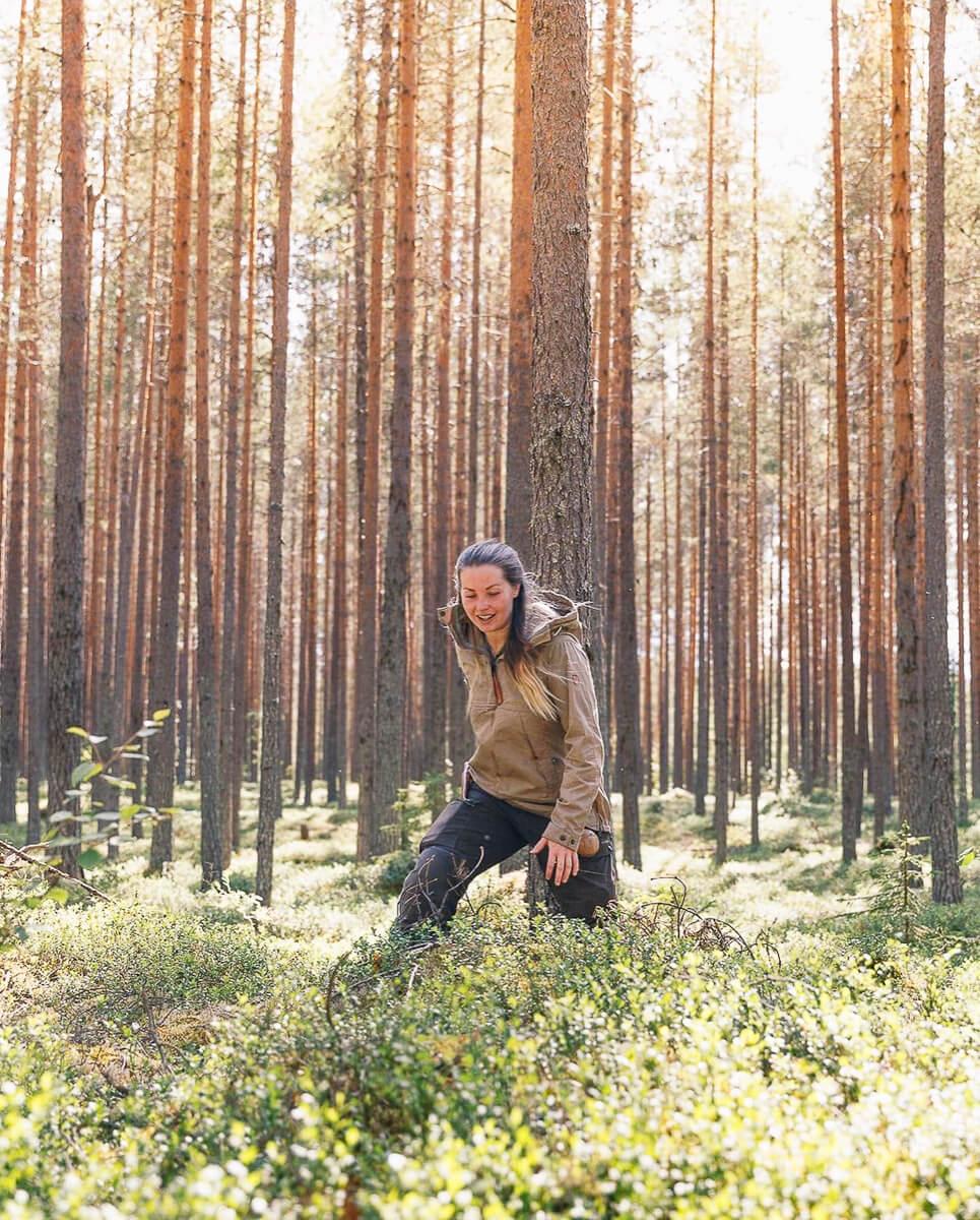 Woman kneeling in a pine forest on a Swedish wilderness adventure holiday