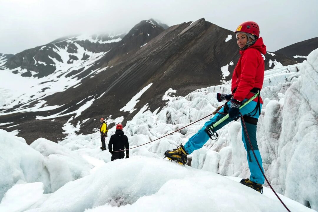 Women glacier hiking in Svalbard, helmeted climbers with ropes on snowy arctic mountain terrain