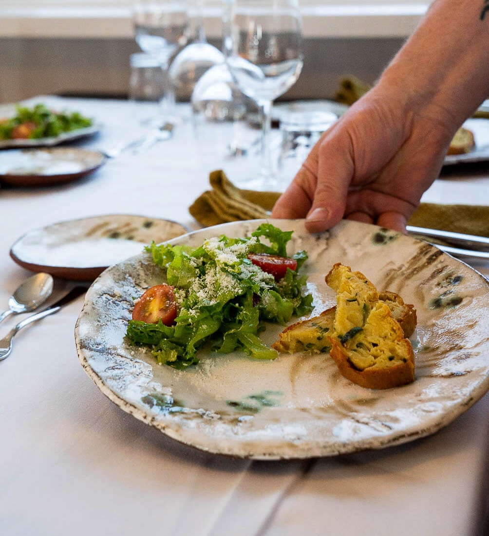 Hand plating food on a ceramic plate at a restaurant dining table with cutlery and glasses