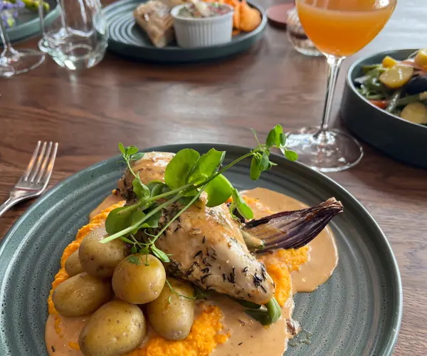 Roast chicken dinner with new potatoes, vegetables and sauce on a plate at a table
