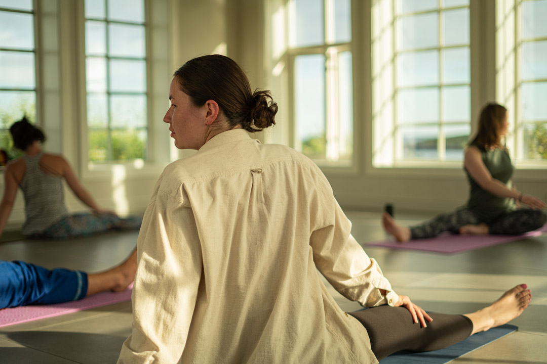 Woman stretching in a yoga studio, seated on a mat in a bright indoor hall