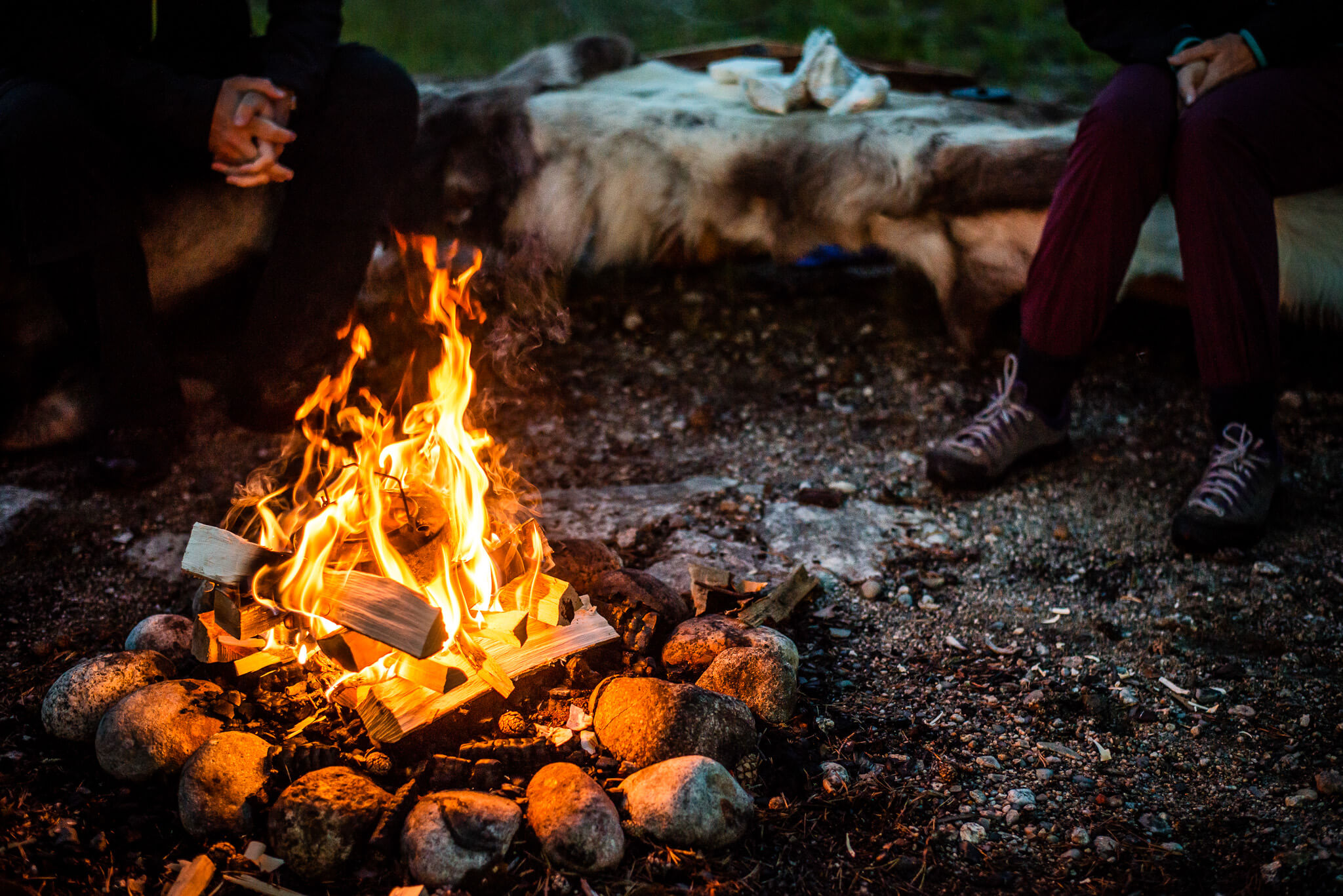 Women sit by a campfire cooking in Swedish Lapland wilderness campsite at night