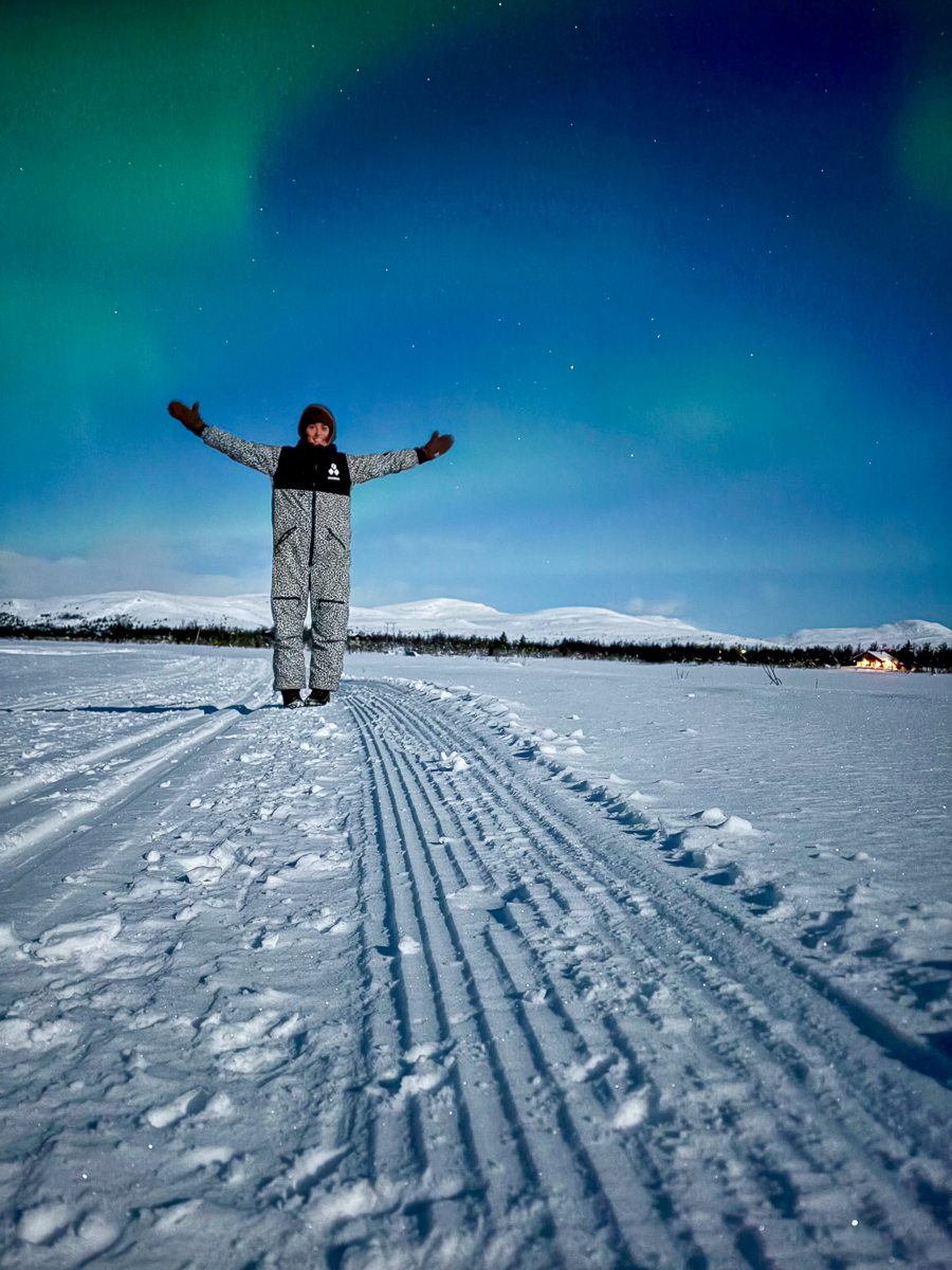 Woman standing on cross-country ski tracks on a snowy landscape under a night sky