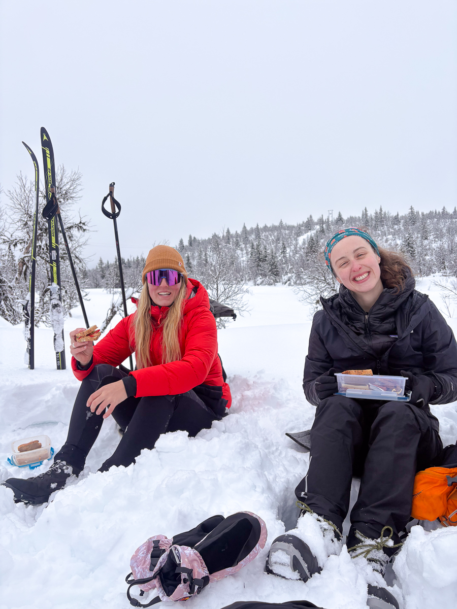 Women cross-country skiing in snowy Norway, relaxing with boots and skis in a winter landscape.