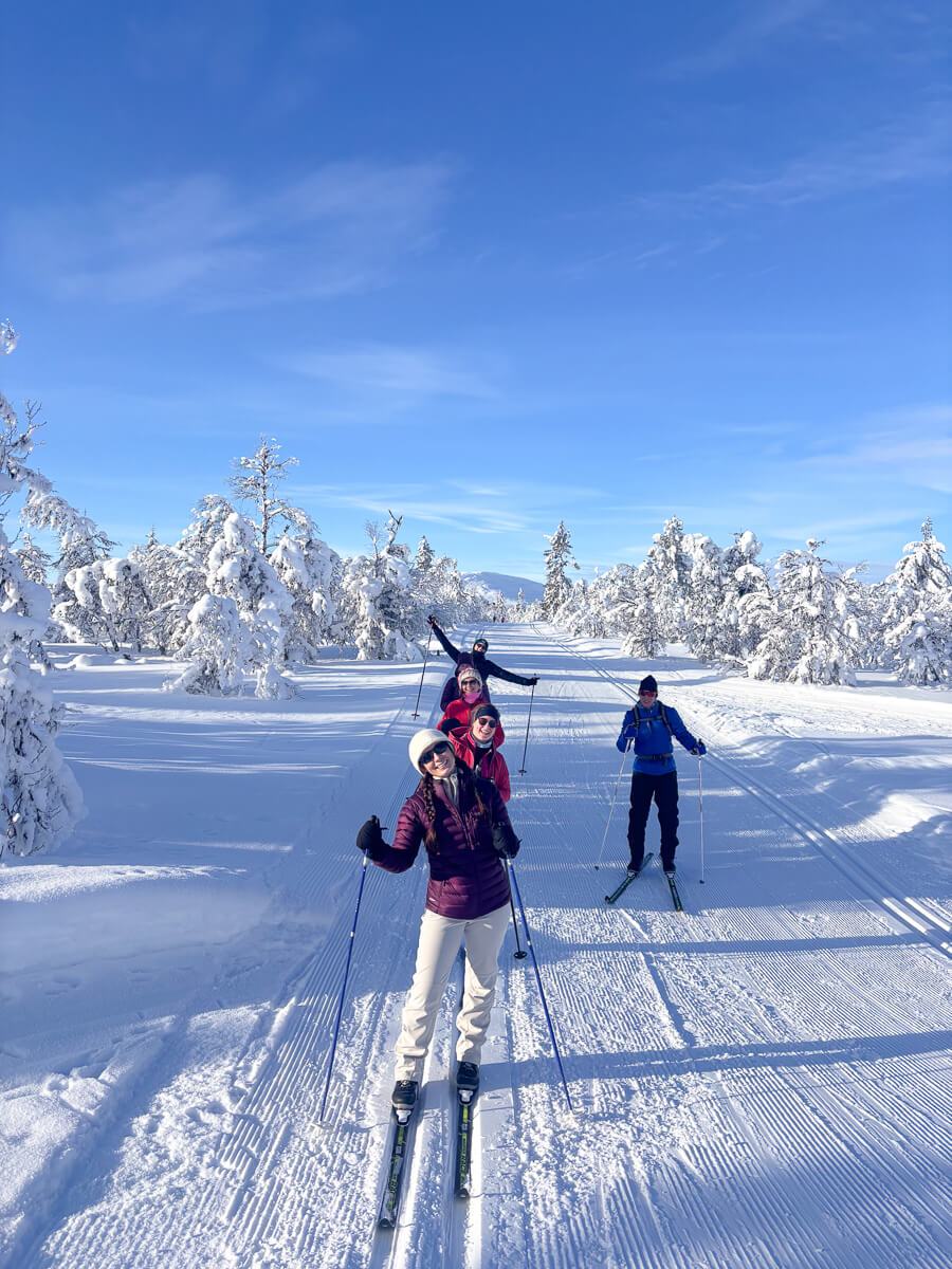 Women cross-country skiing across snowy Norway landscape with pine trees under a clear blue sky