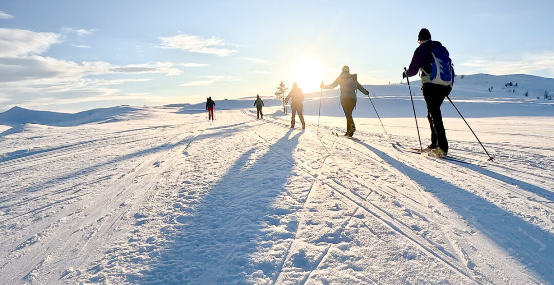 Women cross-country skiing on snowy tracks across a winter mountain landscape at sunrise