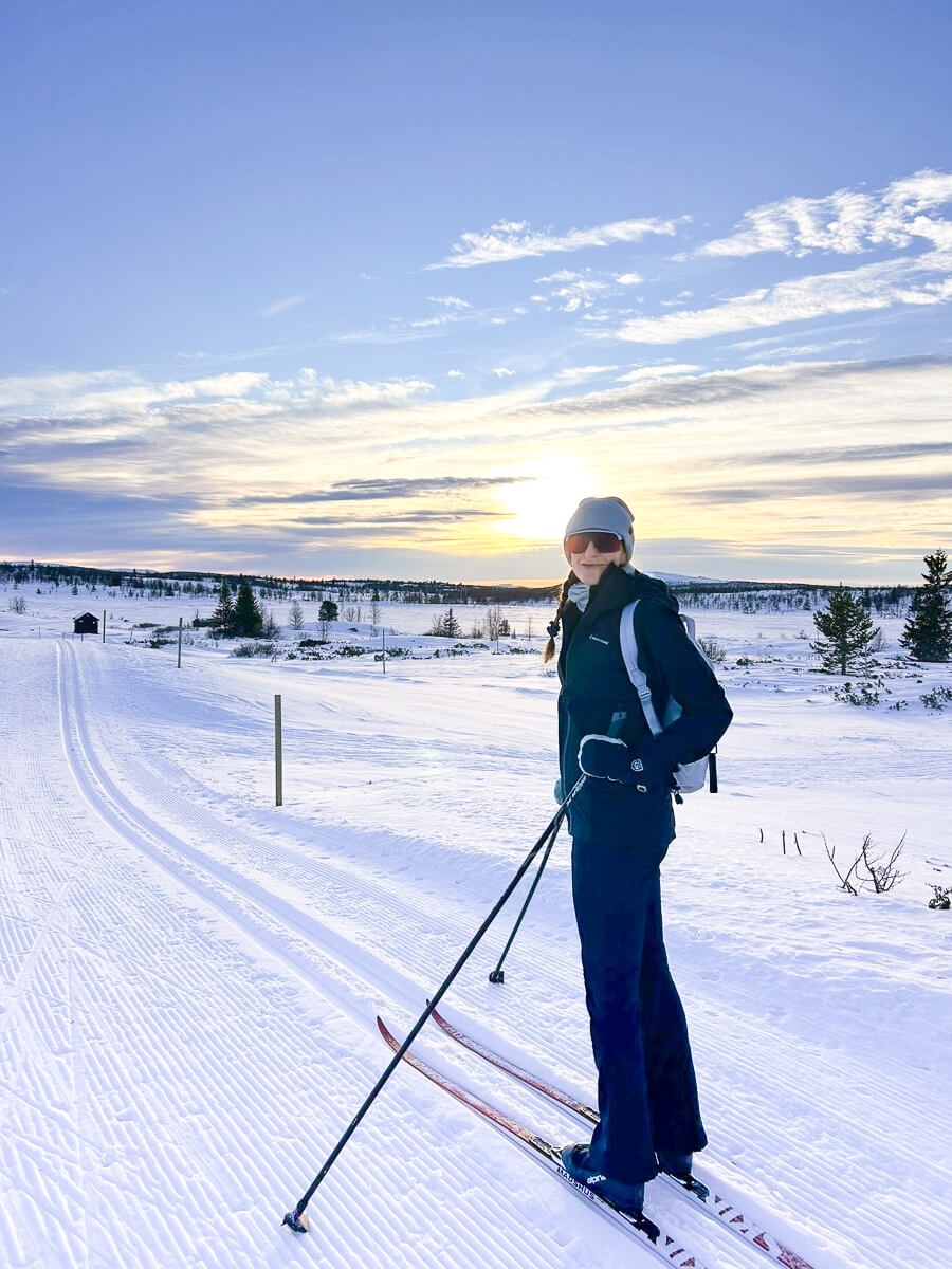 Woman cross-country skiing on a snowy trail in Norway at sunset with skis and poles