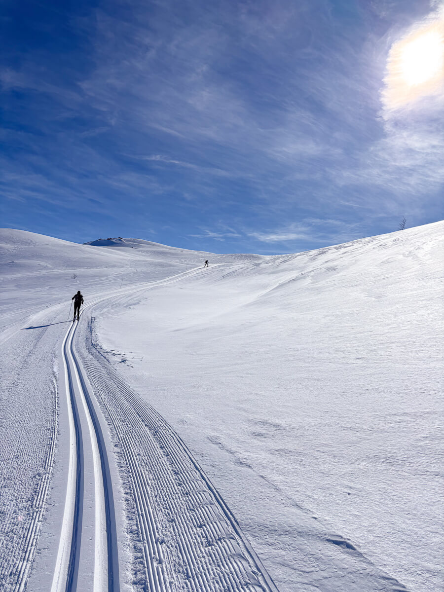 Ski tracks on a snowy mountainside with skiers in Norway under a clear blue sky