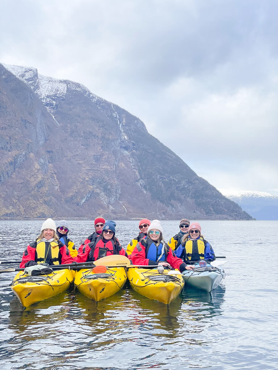 Women in life jackets on yellow kayaks on a snowy Norwegian fjord.