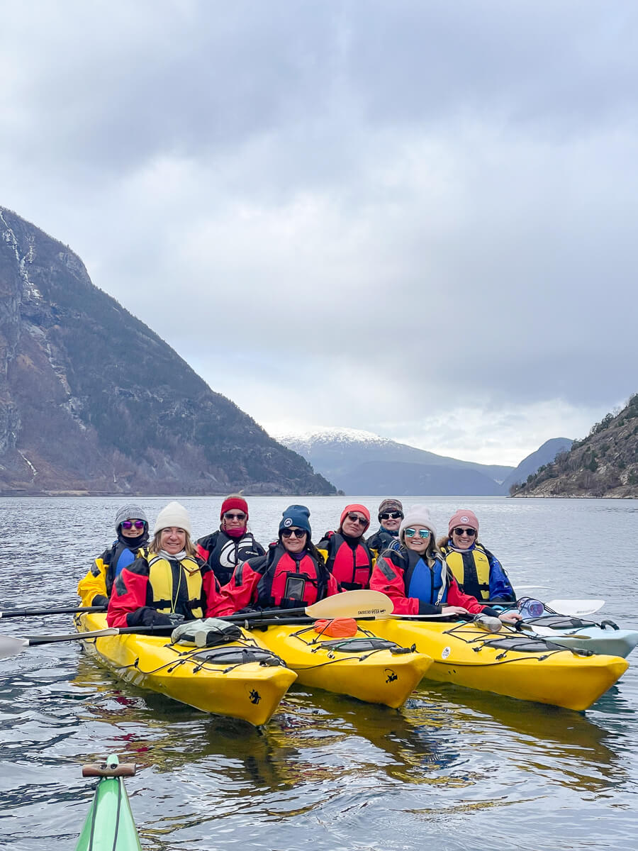Women on yellow kayaks on a fjord in Norway, with snow-capped mountains in the background
