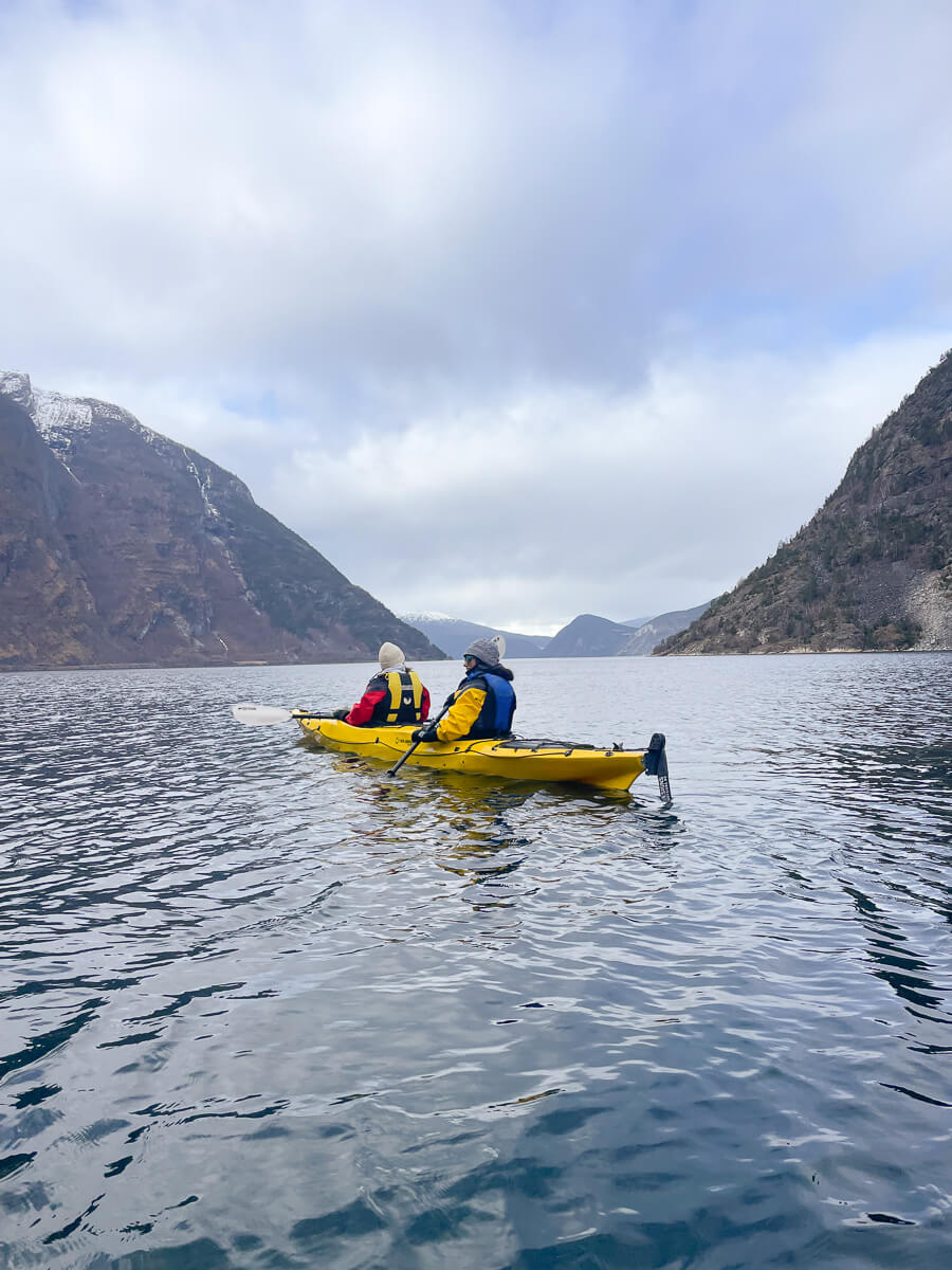 Women kayaking in a Norwegian fjord, paddling on calm water with mountains in the background