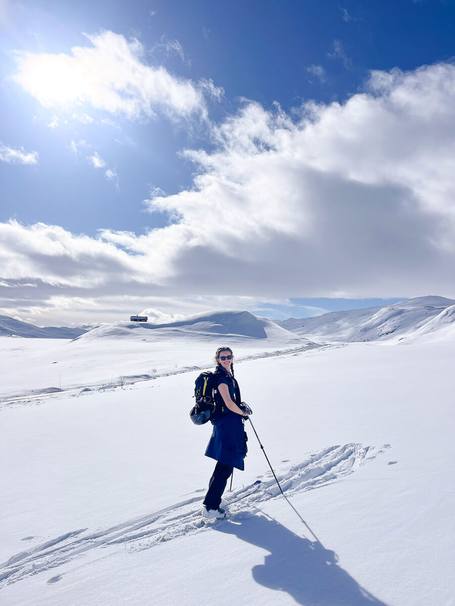 Woman ski touring across a snowy mountain valley under a blue sky with clouds